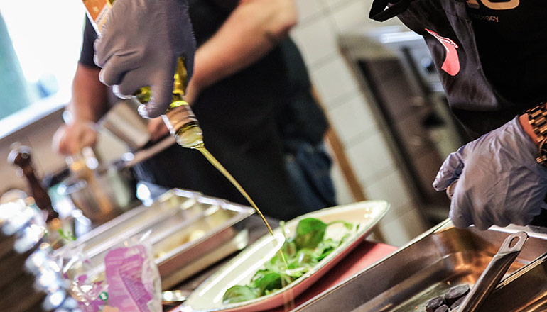 Kockar i kök som häller olja över sallad