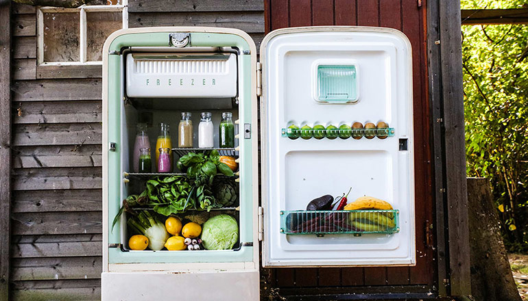 Ett öppet retro kylskåp fyllt med grönsaker utanför gammalt trähus 